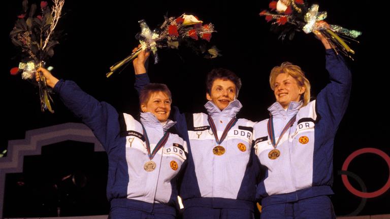 Die Rennrodlerinnen Ute Oberhoffner, Steffi Walter und Cerstin Schmidt jubeln bei der Siegerehrung bei den Olympischen Winterspielen 1988