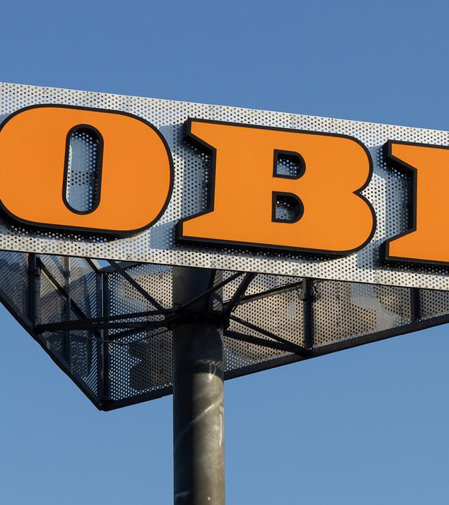 Symbolbild: Weithin sichtbares Firmenschild des Baumarkts OBI auf einem Pylonmast vor blauem Himmel. 