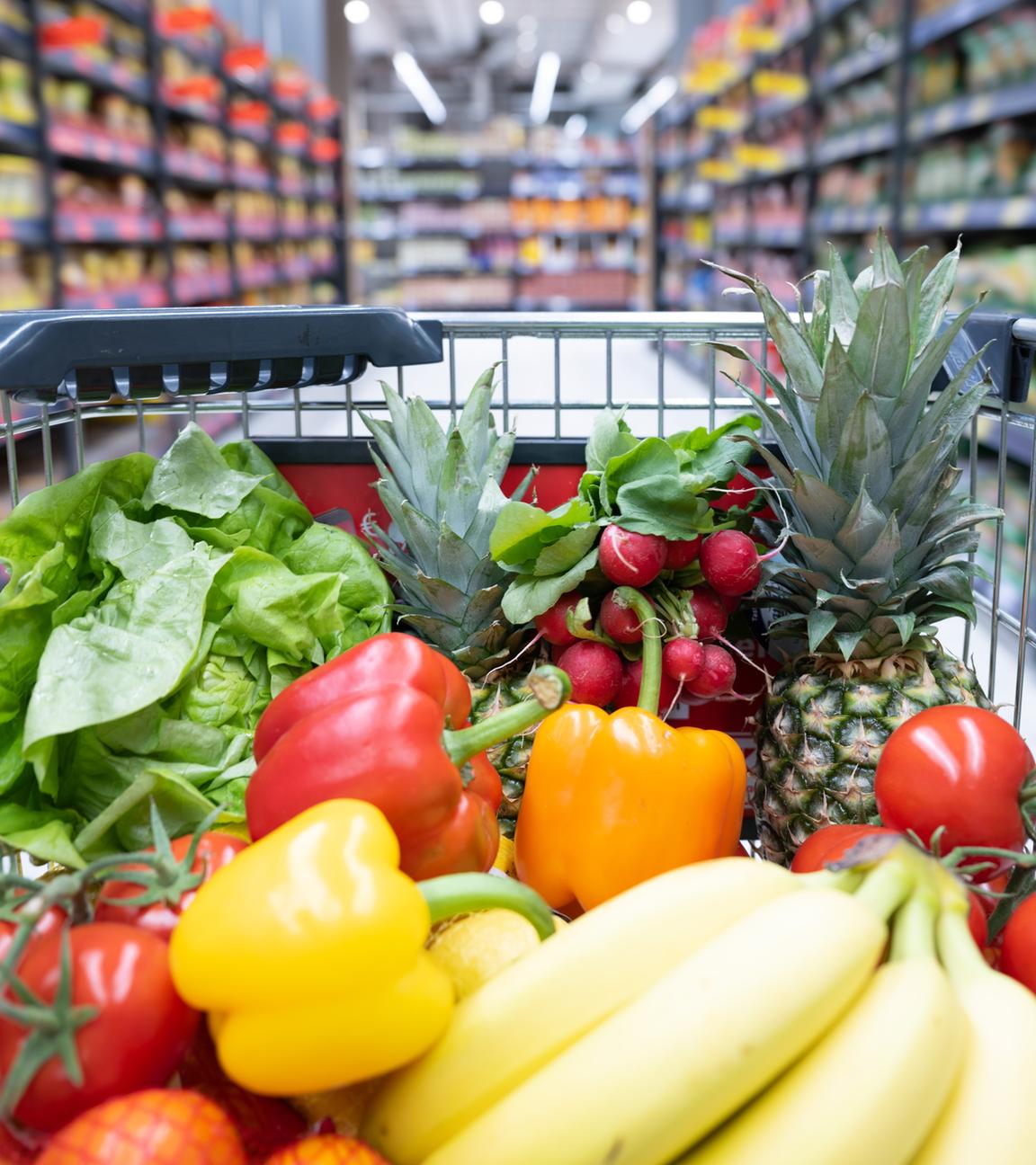 Ein Einkaufskorb mit Obst und Gemüse steht in einem Supermarkt.