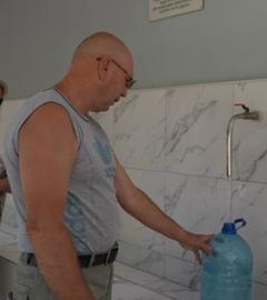Zwei Personen füllen an Wasserhähnen Wasser in Kanister ab.