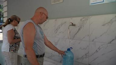 Zwei Personen füllen an Wasserhähnen Wasser in Kanister ab.