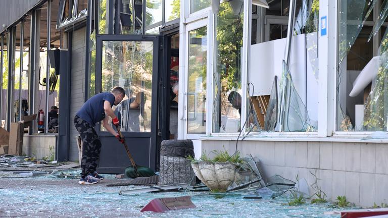 zerstörtes Ladenfenster und Mann mit Besen