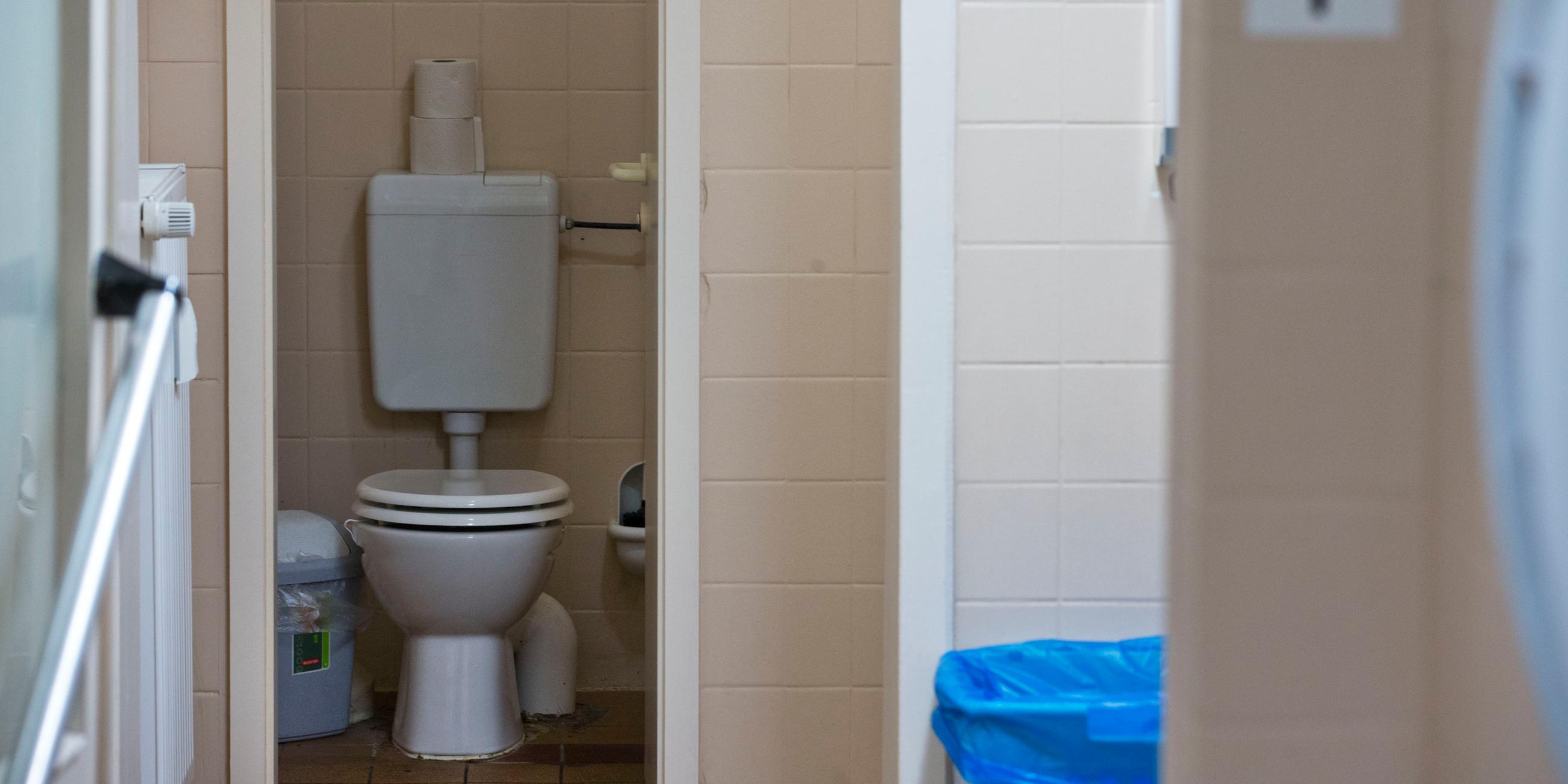 Rosa geflieste öffentliche Toilette mit geöffneter Tür zur Klokabine.