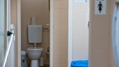 Rosa geflieste öffentliche Toilette mit geöffneter Tür zur Klokabine.