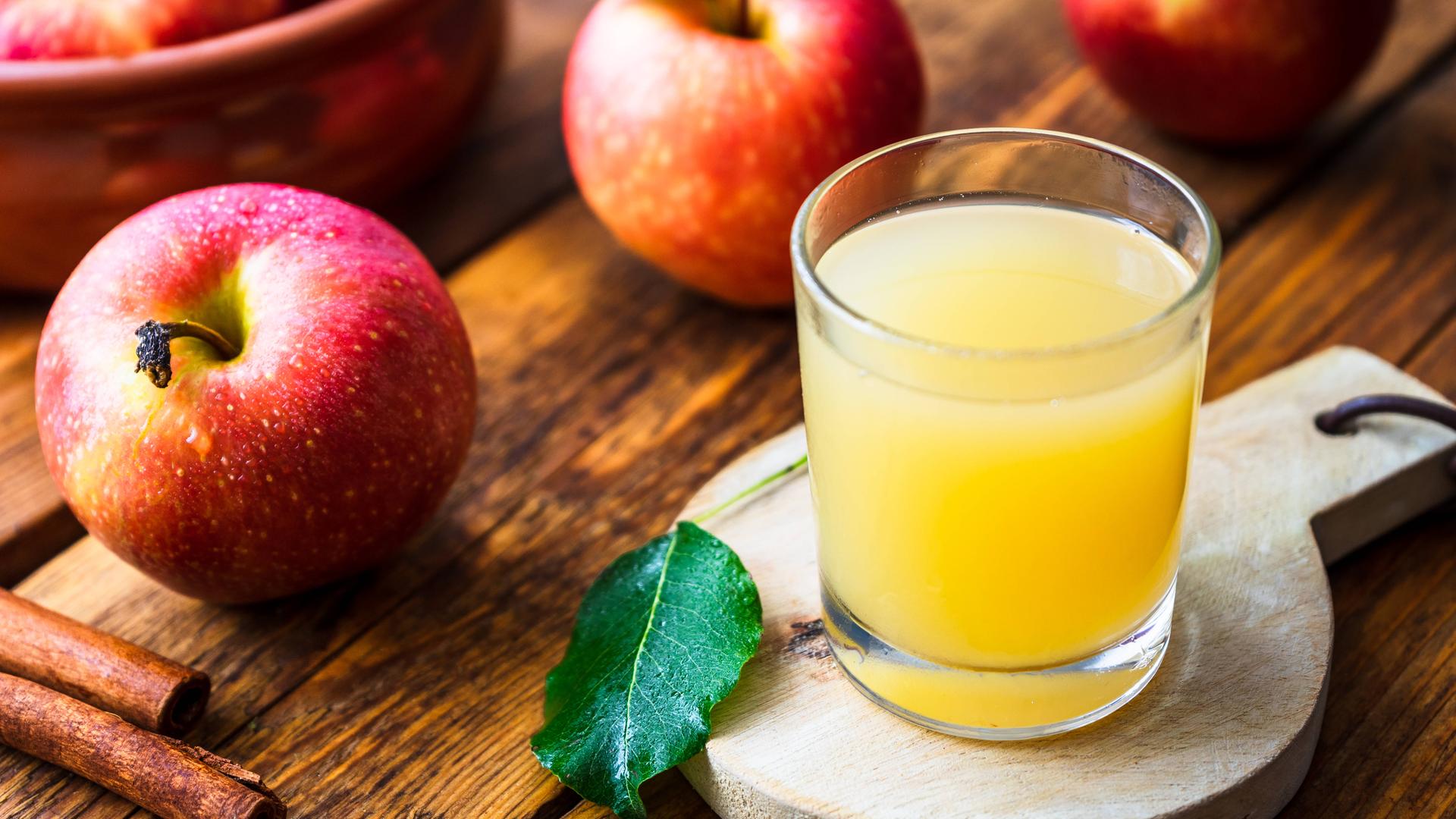 Ein Glas mt naturtrübem Apfelsaft steht af einem Brettchen, drumherum liegen Äpfel.