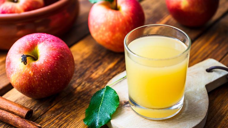 Ein Glas mt naturtrübem Apfelsaft steht af einem Brettchen, drumherum liegen Äpfel.