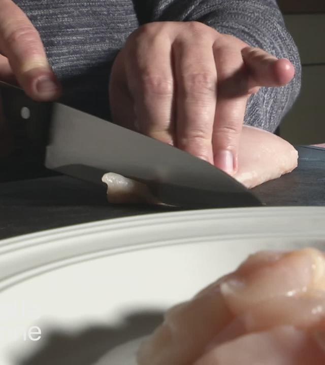Frau schneidet Hähnchenfleisch