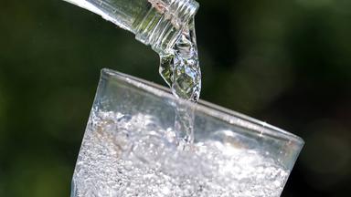 Mineralwasser wird aus einer Flasche in ein Glas gegossen.