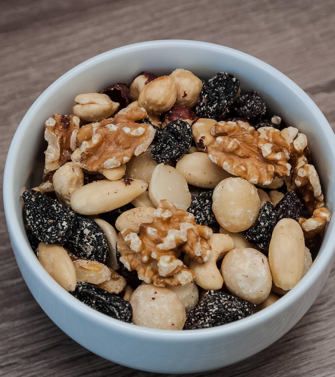 Eine kleine weiße Schüssel, die mit Studentenfutter gefüllt ist, steht auf einer Holzoberfläche.