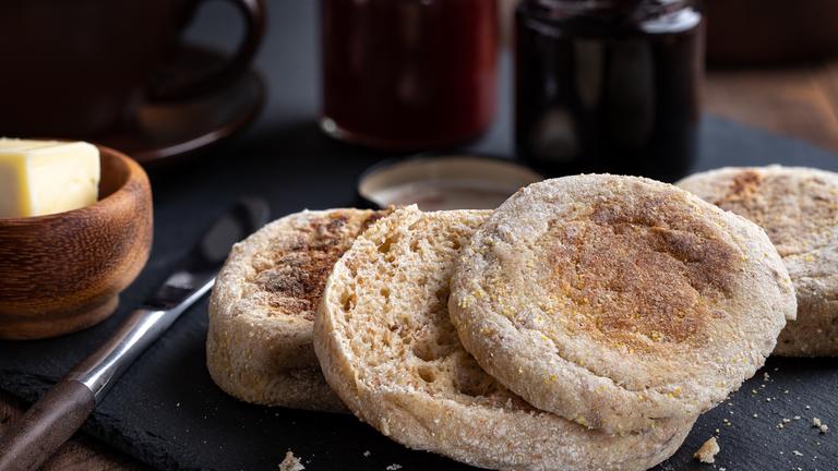 Toast-Brötchen liegen aufgeschnitten auf einem Brett, daneben Butter, dahinter Marmelade.
