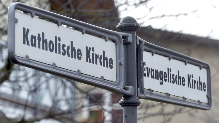 "Evangelische / Katholische Kirche" - ein Wegweiser in Kühlungsborn zeigt in die beiden Richtungen, in denen sich die verschiedenen Kirchen befinden