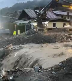 Einsatzkräfte und ein Bagger stehen vor einem reissenden Wasserlauf