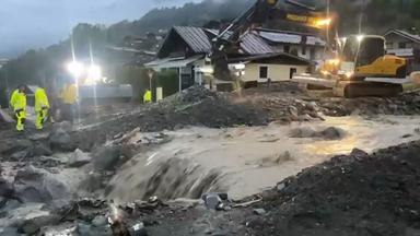 Einsatzkräfte und ein Bagger stehen vor einem reissenden Wasserlauf