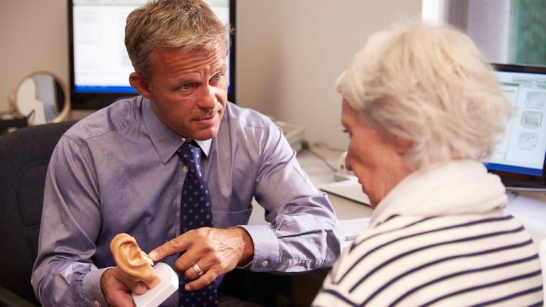 Ohrenarzt benutzt zur Veranschaulichung ein Ohr-Modell im Gespräch mit älterer Patientin.