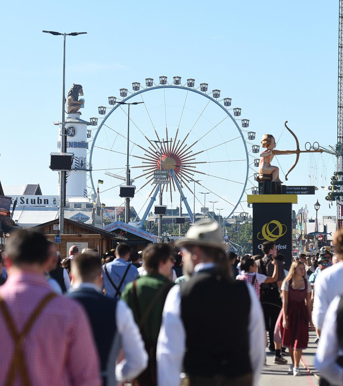 Besucher strömen über das Oktoberfest, im Hintergrund ist ein Riesenrad zu sehen.