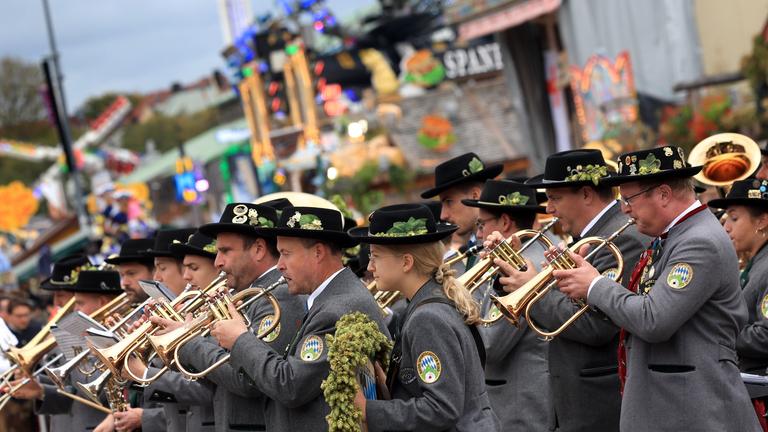 Bayerische Musikanten stehen am letzten Tag des Oktoberfestes unter bewölktem Himmel auf dem Festgelände.
