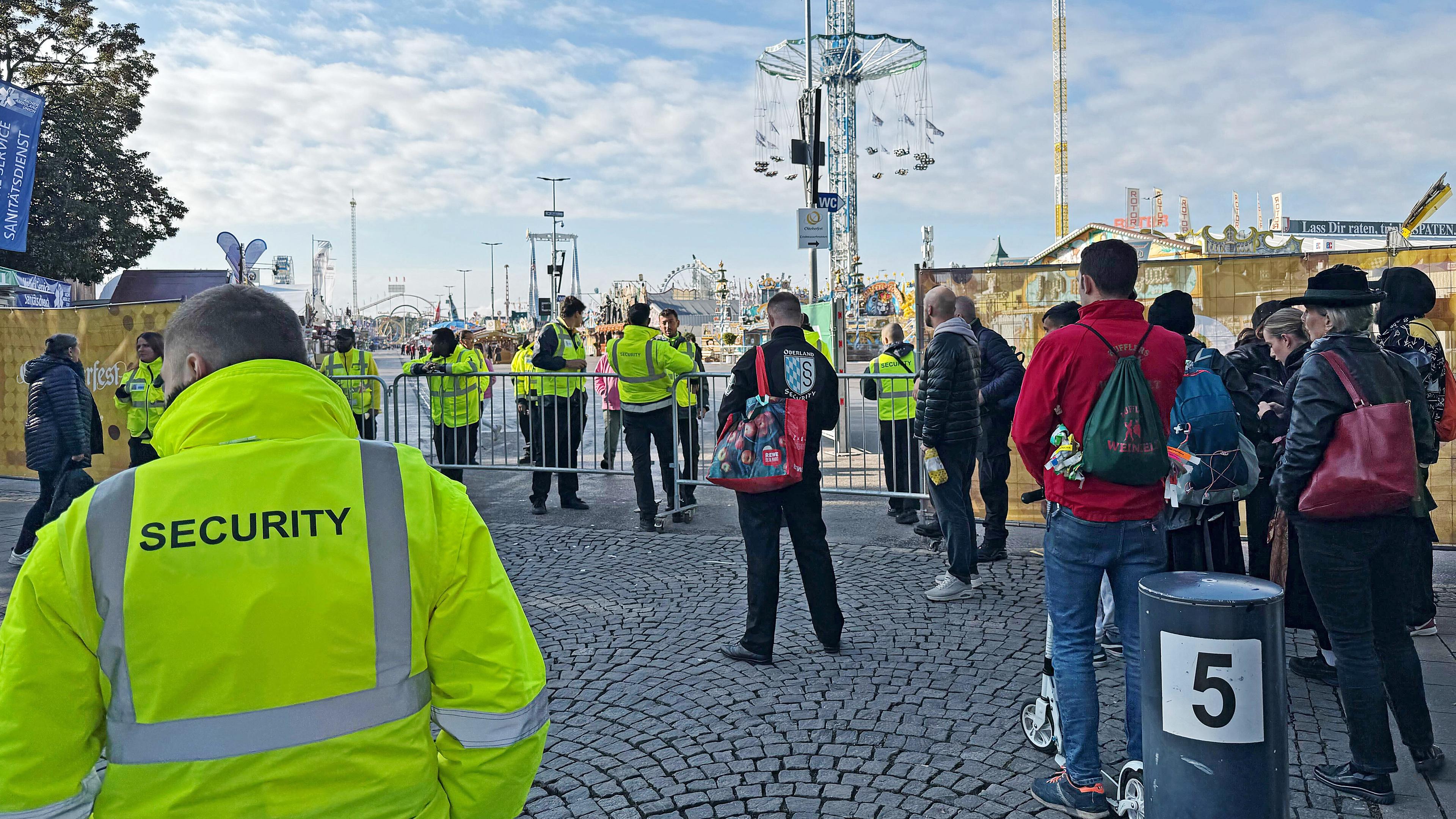 Menschen stehen an einer Absperrung an einem Eingang zum Oktoberfest am 01.10.2025