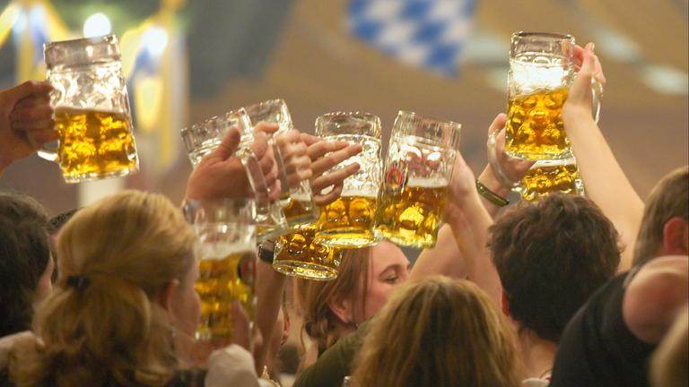 Viele Personen in Tracht halten Bierkrüge in die Höhe auf dem Oktoberfest in München.