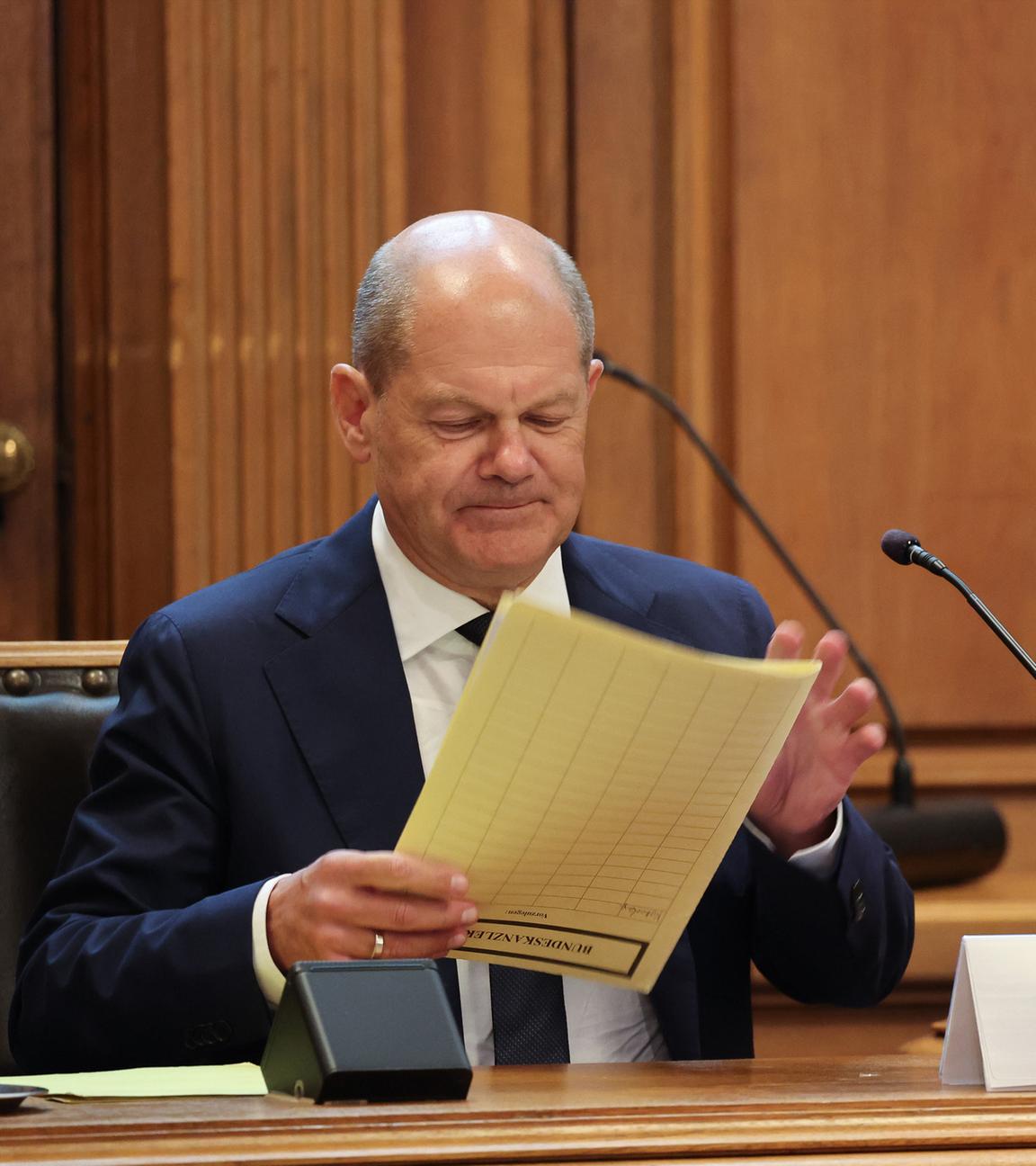 Bundeskanzler Olaf Scholz (SPD) sitzt auf seinem Platz auf der Senatsbank mit einem Plastikschild mit dem Text ·Olaf Scholz Zeuge· vor Beginn einer Sitzung des Parlamentarischen Untersuchungsausschusses ·Cum-Ex· im Plenarsaal der Hamburgischen Bürgerschaft im Rathaus. 