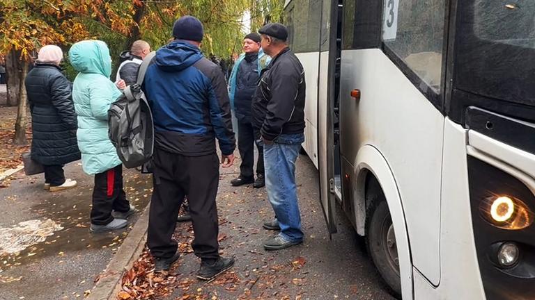 Menschen stehen am 30.10.2026 in Oleschky, Ukraine, an einem Bus.