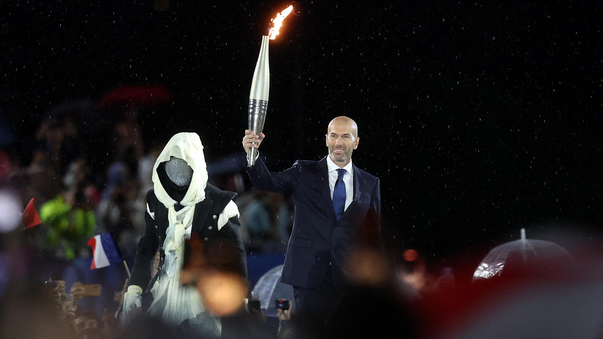 Zinedine Zidane, ehemaliger französischer Fußballspieler und -manager, hält die olympische Fackel