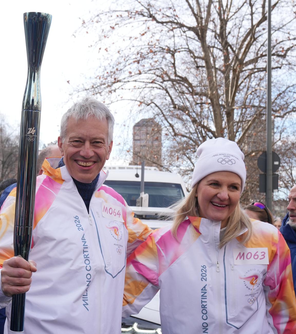 Olympia, Olympische Winterspiele Mailand Cortina 2026, IOC-Präsidentin Kirsty Coventry (r) und James Quincey, CEO von Coca-Cola, stehen bei der Übergabe der olympischen Fackel nebeneinander.