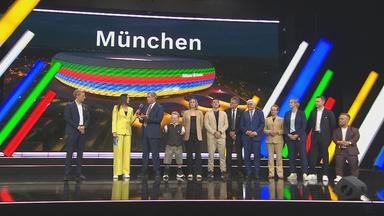 Auf der Bühne wird verkündet, dass München sich als Austragungsort für Olympia bewirbt.