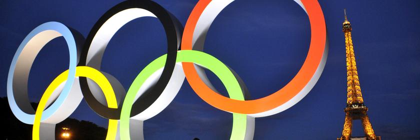Die beleuchteten olympischen Ringe im Vordergrund. Im Hintergrund der Eiffelturm beleuchtet.