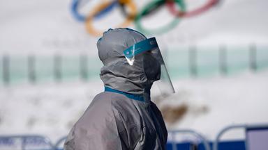Eine Person steht im Schutzanzug vor den olympischen Ringen
