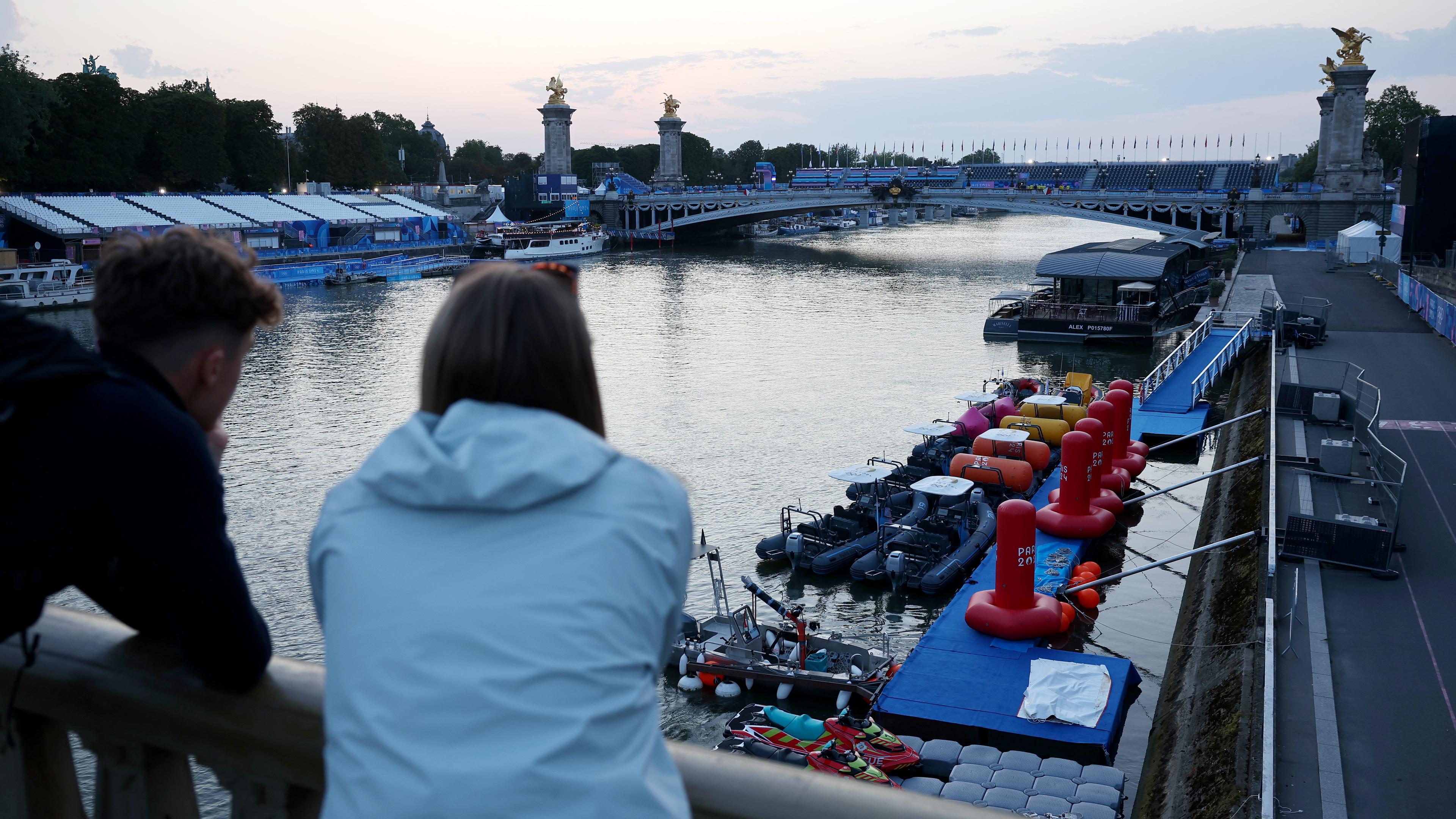 Olympia, Paris 2024; Zwei Personen blicken auf die Seine, nachdem der Triathlon der Männer verschoben wurde.