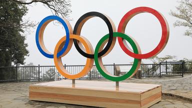 Die Olympischen Ringe in fünf verschiedenen Farben auf einem Holzpodest