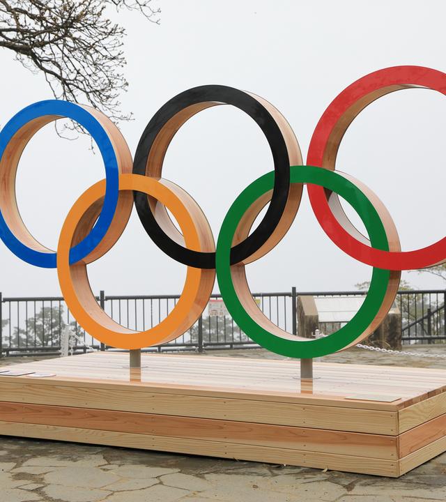 Die Olympischen Ringe in fünf verschiedenen Farben auf einem Holzpodest