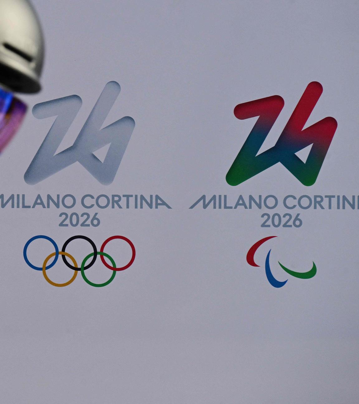 Im Vordergrund steht eine Skifahrerin. Hinter ihr sieht man zwei Mal das Logo der Olympischen Winterspiele.