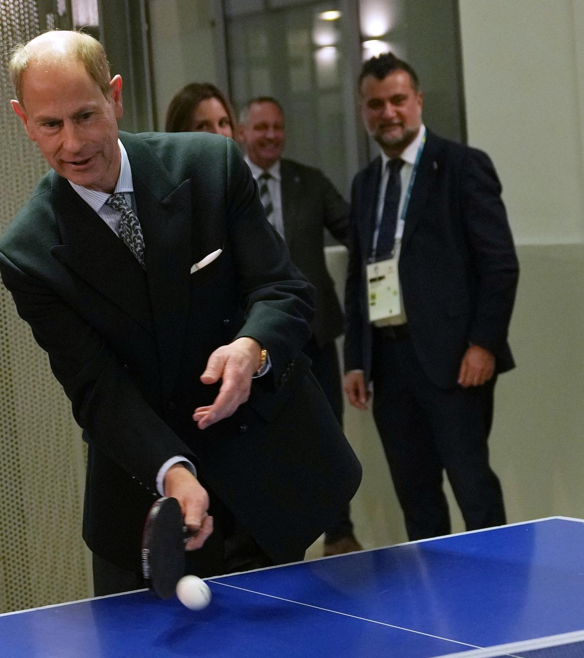 Prinz Edward steht an einer Tischtennis-Platte und schlägt einen Ball auf.