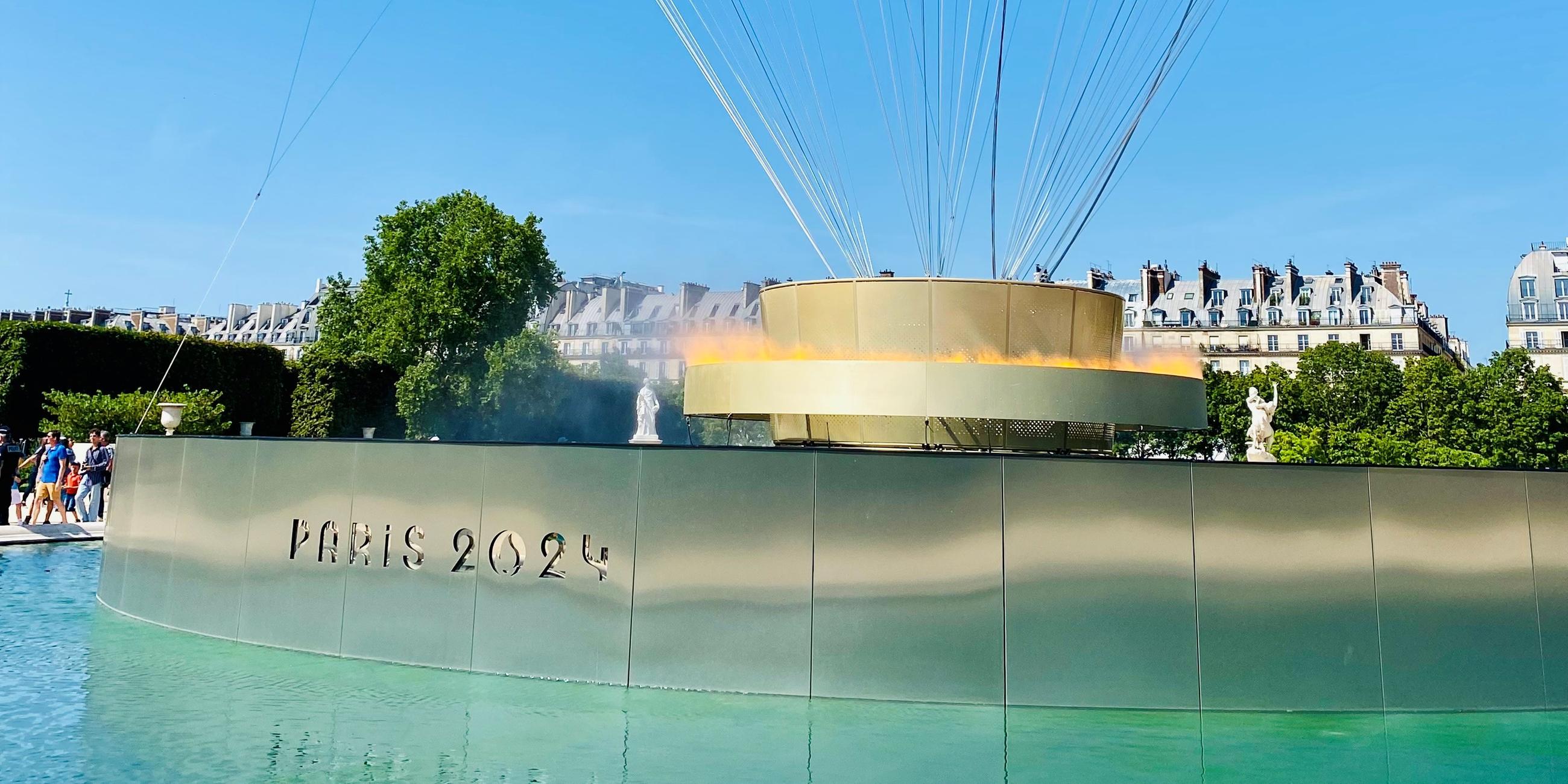 In der Mitte eines Wasserbeckens halten kreisförmige Flammen einen goldenen Heißluftballon empor.
