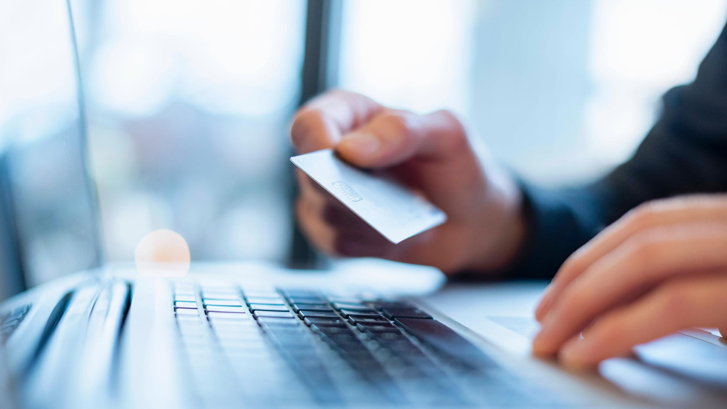 Ein junger Mann hält eine Kreditkarte über der Laptoptastatur in den Händen.