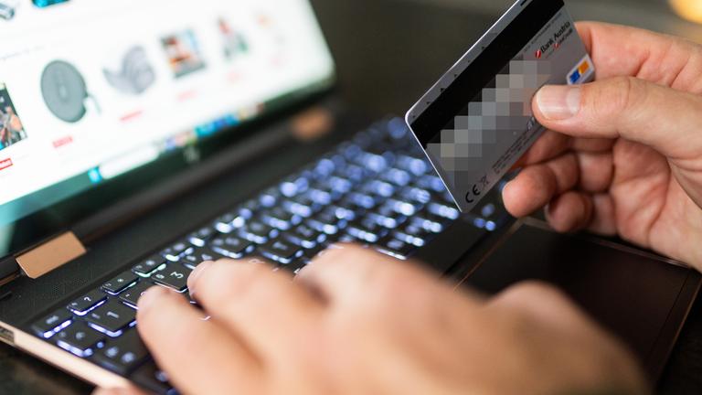 Ein Person sitzt mit Kreditkarte vor dem Laptop und gibt die Kreditkarteninformationen ein.