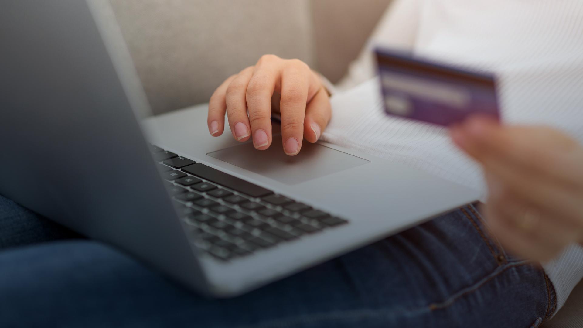 Eine Frau sitzt mit einem Laptop und einer Kreditkarte auf der Couch