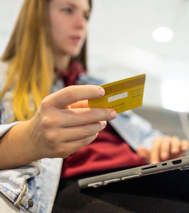 Eine Frau hat ihren Laptop auf dem Schoß und hält eine Kreditkarte in der Hand.