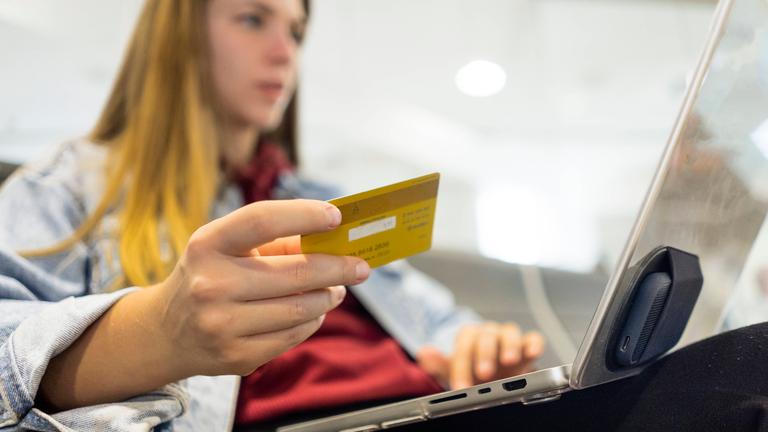 Eine Frau hat ihren Laptop auf dem Schoß und hält eine Kreditkarte in der Hand.
