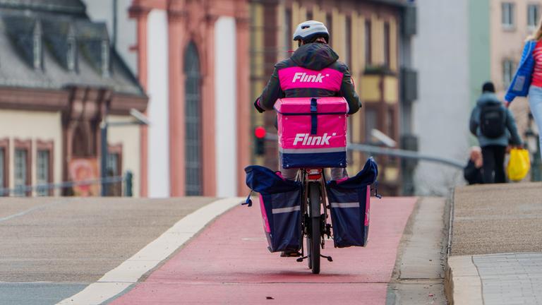 Ein Mitarbeiter des Lieferdienstes "Flink" radelt am 22.03.2024 über die Alte Brücke in Frankfurt am Main.