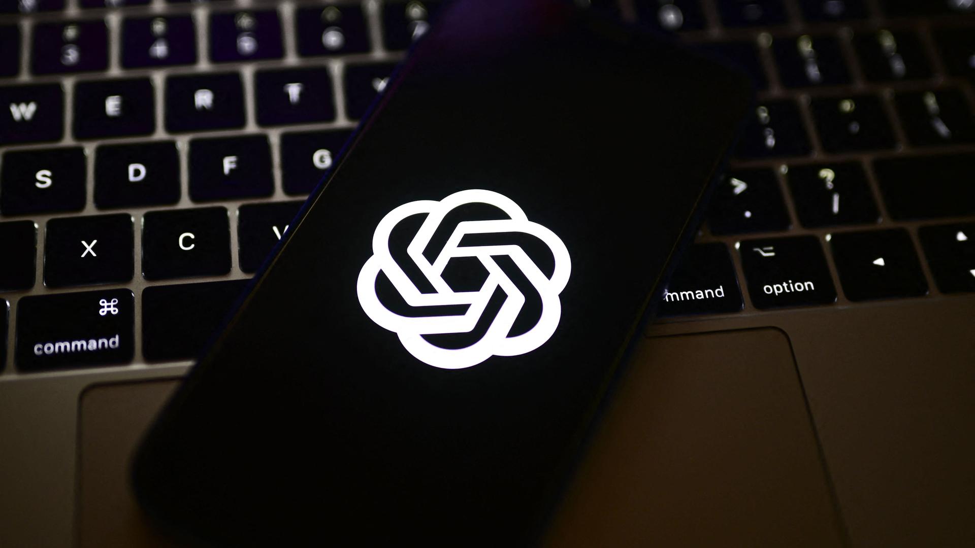 Ein Smartphone mit dem Logo von OpenAI wird über ein Apple MacBook gehalten.