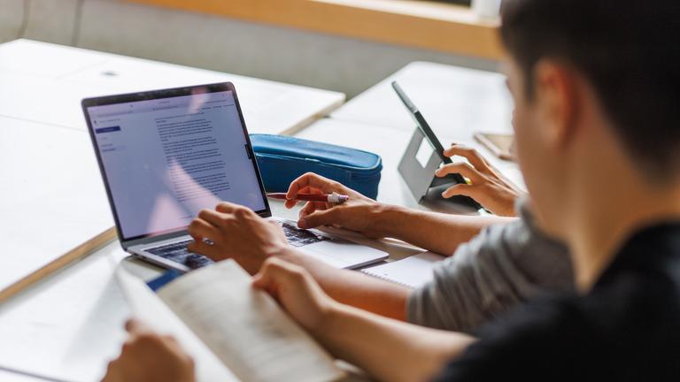 Schüler eines Gymnasiums sitzen vor einem Computer und benutzen ein KI-Tool.