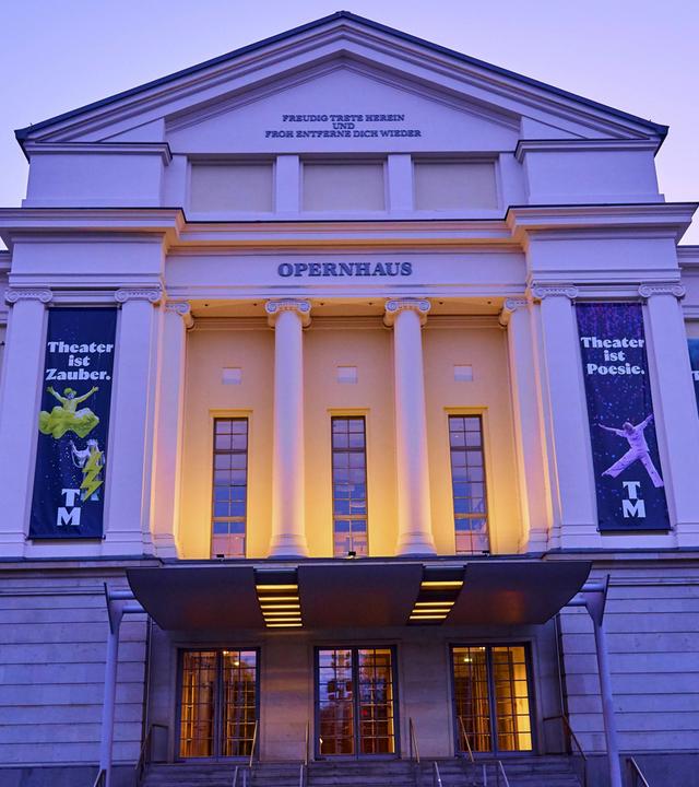 Beleuchtete Fassade eines historischen Opernhauses in der Abenddämmerung.