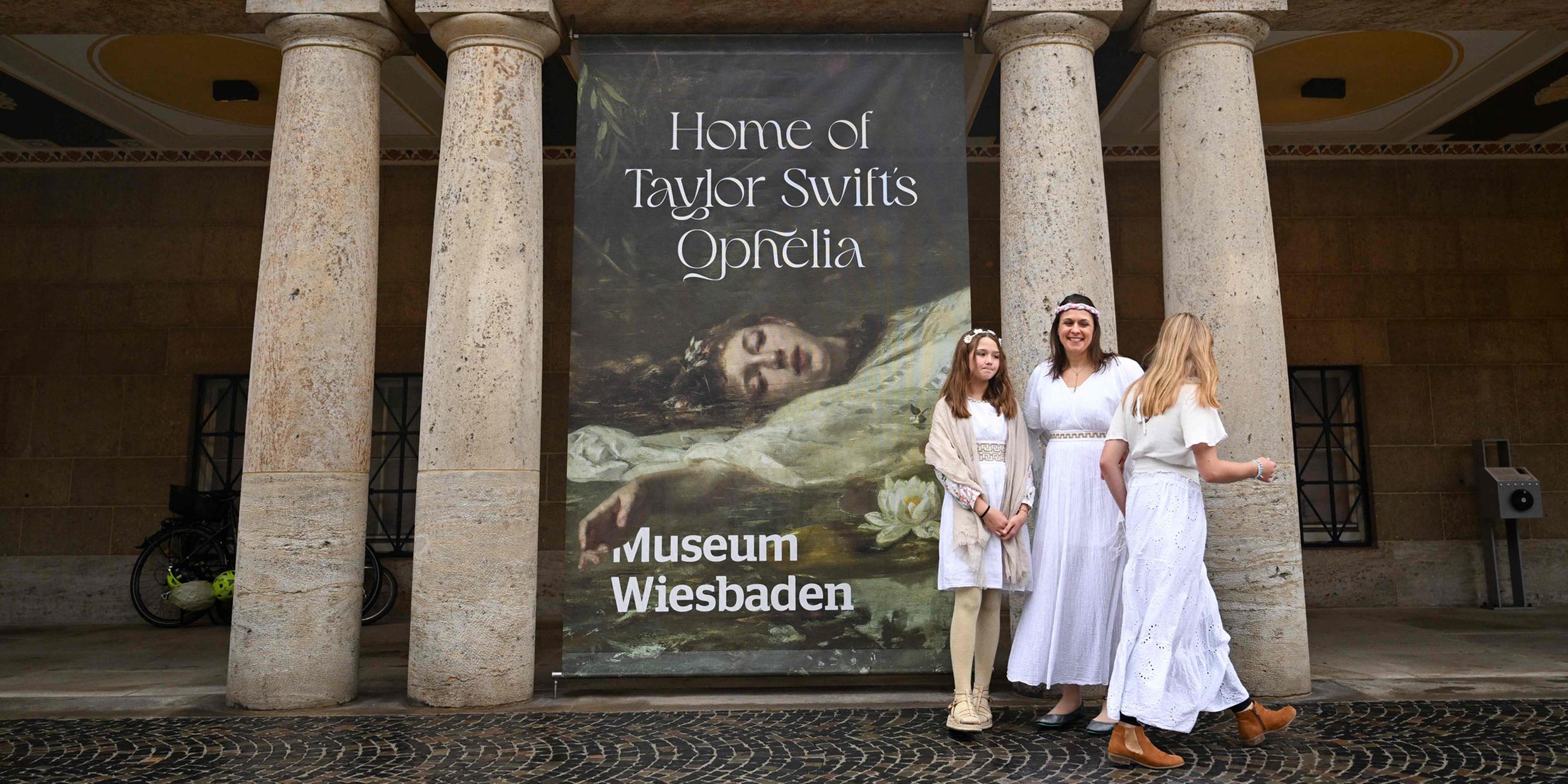 Fans der US-Sängerin Taylor Swift posieren vor dem Plakat "Home of Taylor Swift’s Ophelia“ vor dem Museum in Wiesbaden.