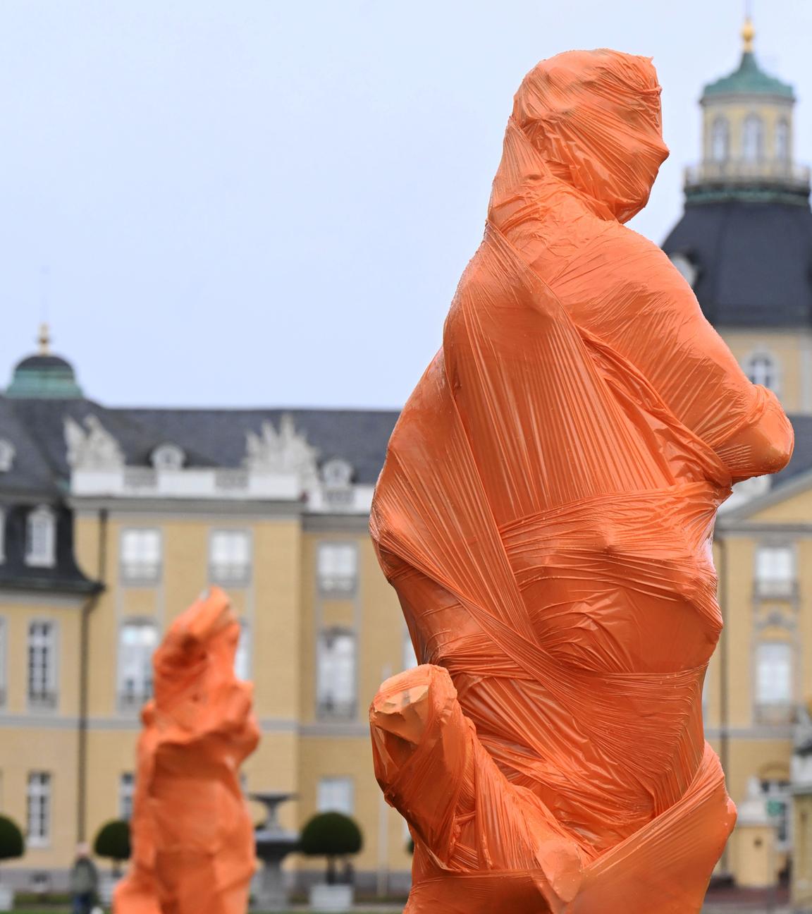 Vor dem Karlsruher Schloss haben Mitglieder des Künstlerkollektivs Francis Karat mehrere Skulpturen mit orangefarbener Folie verhüllt.