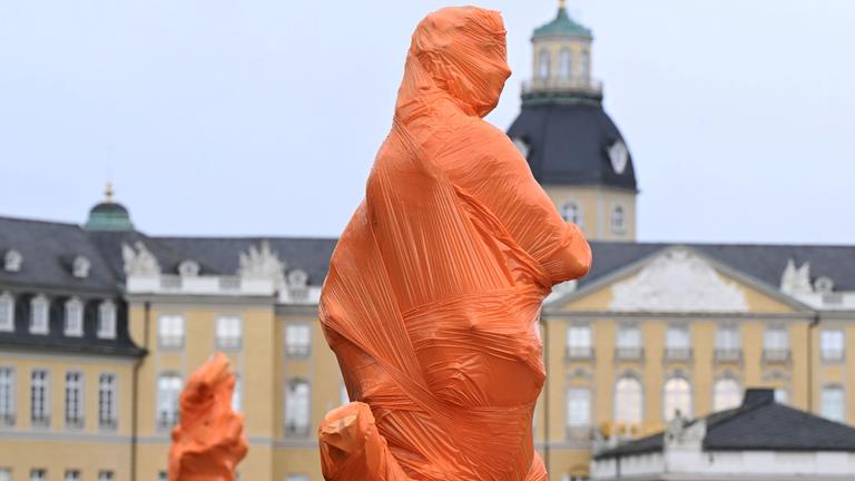 Vor dem Karlsruher Schloss haben Mitglieder des Künstlerkollektivs Francis Karat mehrere Skulpturen mit orangefarbener Folie verhüllt.