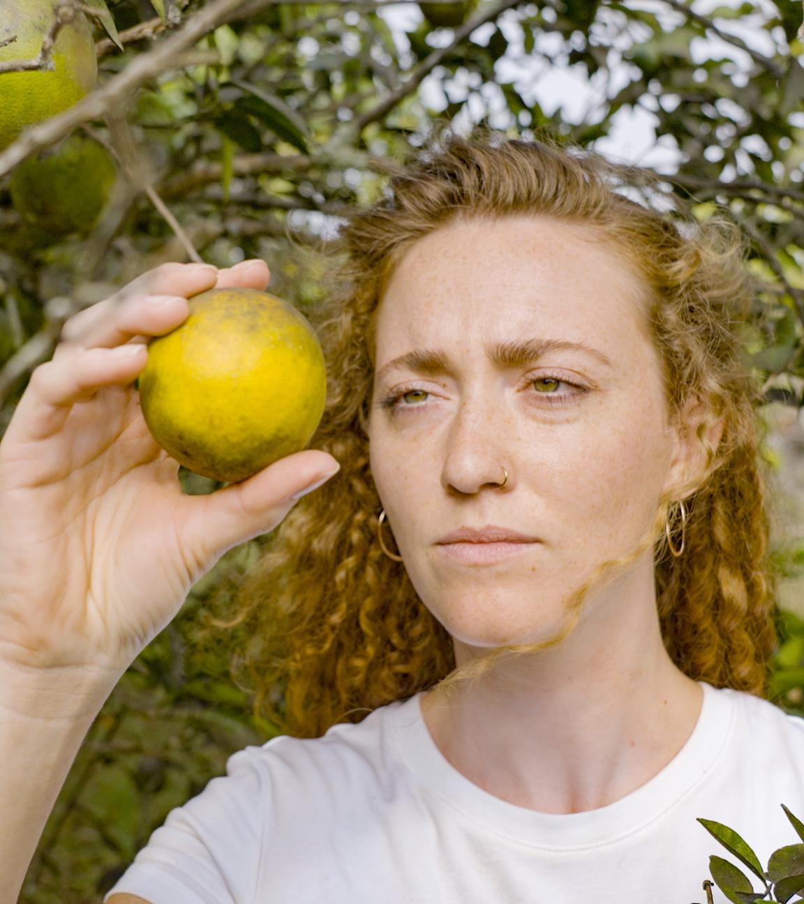 Eine Frau hält eine unreife Orange an einem Orangenbaum in der Hand.