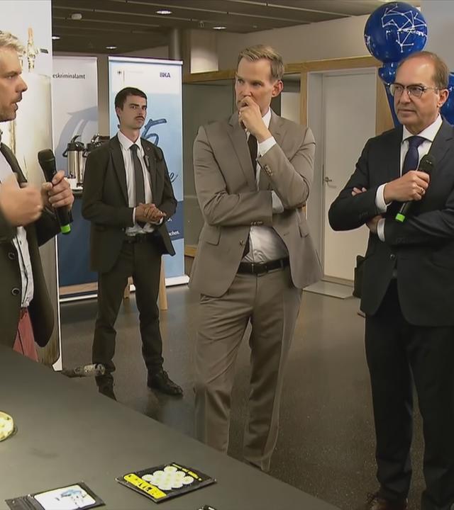 Zu sehen ist Alexander Dobrindt der von mehreren Personen umringt ist und eine Person erklärt was 