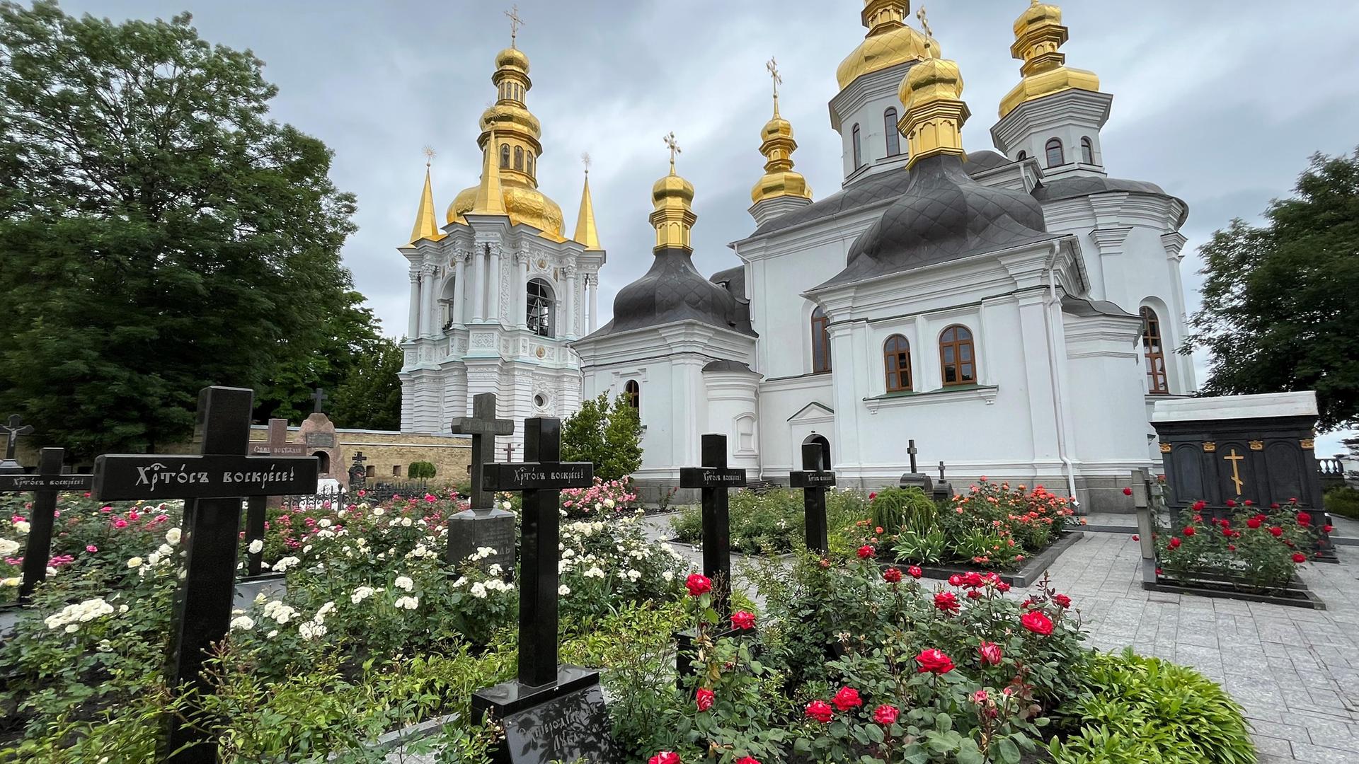 Ukraine, Kiew: Auf dem Gelände des Höhlenklosters stehen Kirchengebäude und auf einem Friedhof mit Gräbern Kreuze.